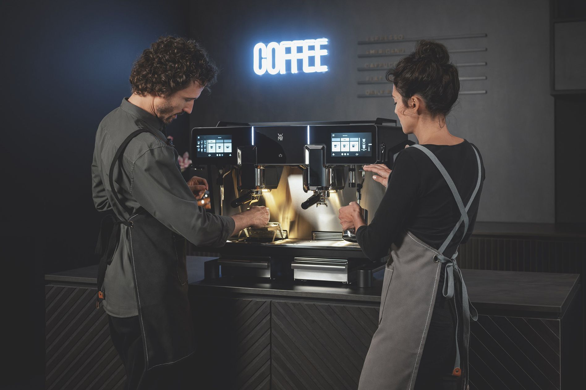 Man and woman using a WMF espresso NEXT portafilter machine in parallel